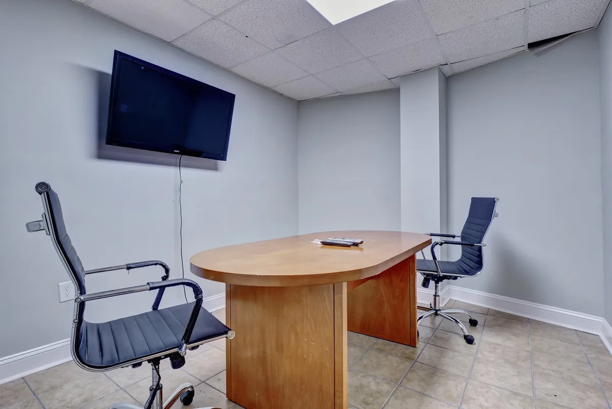 A focused business environment with a wooden conference table, two ergonomic office chairs, and a flat-screen TV for presentations or virtual meetings. The setting is professional yet comfortable, perfectly suited for remote work, small meetings, or brainstorming sessions.