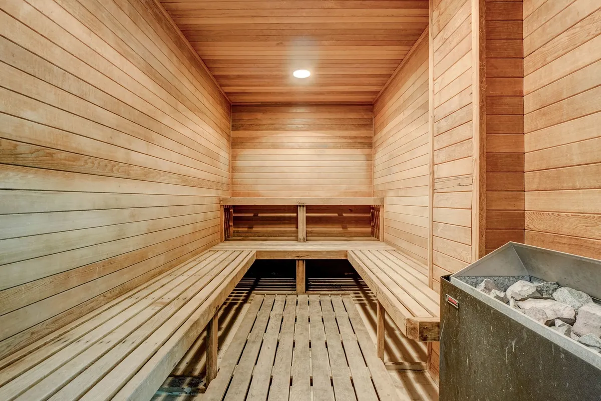 A tranquil sauna space with wooden benches and a central stone heater, surrounded by wooden walls. The atmosphere is warm and serene, inviting guests to unwind and rejuvenate.