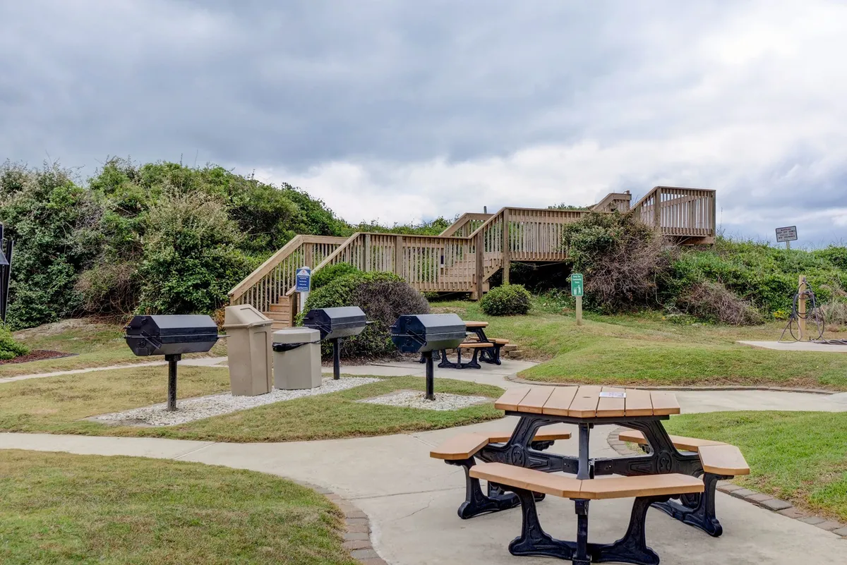This scene highlights the outdoor barbecue area, with picnic tables, grills, and a staircase leading up to the property. The area invites families to gather for meals and enjoy relaxed outdoor dining after a day of play.