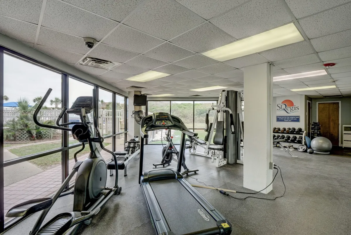 A bright, modern fitness center featuring a treadmill, elliptical, weight machines, free weights, and large windows that let in ample natural light. The room conveys a sense of energy and motivation for an active lifestyle.