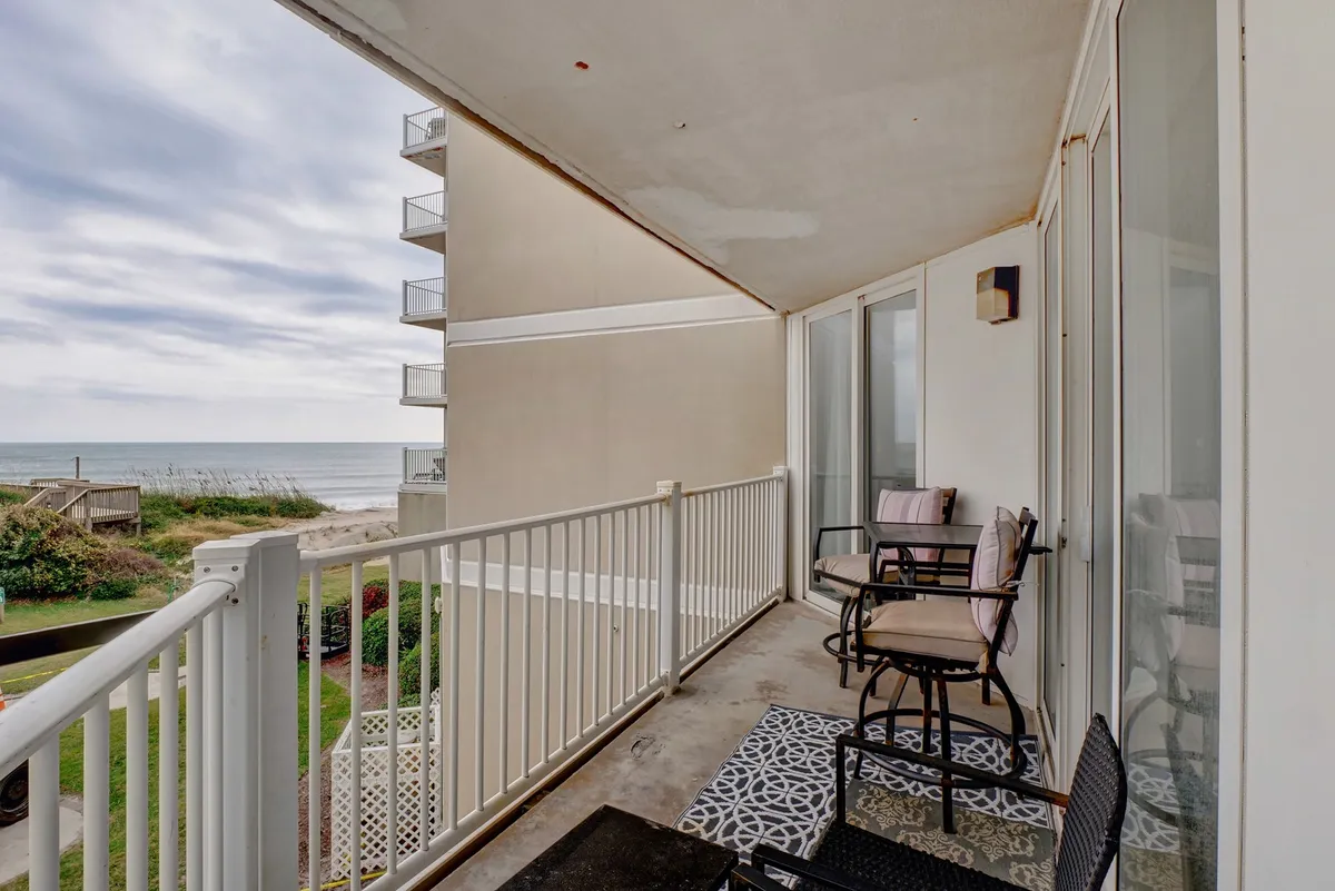 The image showcases a balcony with a clear view of the ocean. The balcony features a stylish railing, a comfortable seating area, and is bathed in soft natural light. The angle captures the inviting spot for morning coffee or evening relaxation, with the tranquil ocean stretching beyond.