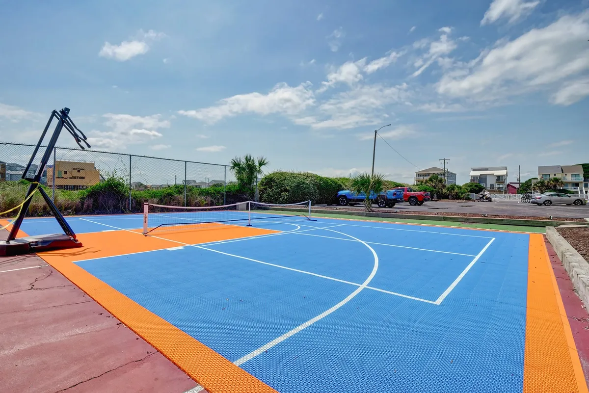This exterior scene captures a vibrant multi-use court featuring a basketball hoop and tennis net set against a colorful surface. The open sky and greenery around the court convey a sense of outdoor fun and active recreation, inviting friendly matches and group sports.