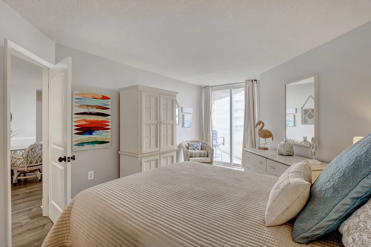 A tranquil master bedroom scene featuring a comfortable bed with textured bedding, an art piece on the wall, a window allowing natural light to filter in, and a cozy chair in the corner. The room exudes a calm, restful atmosphere ideal for a restorative night's sleep.