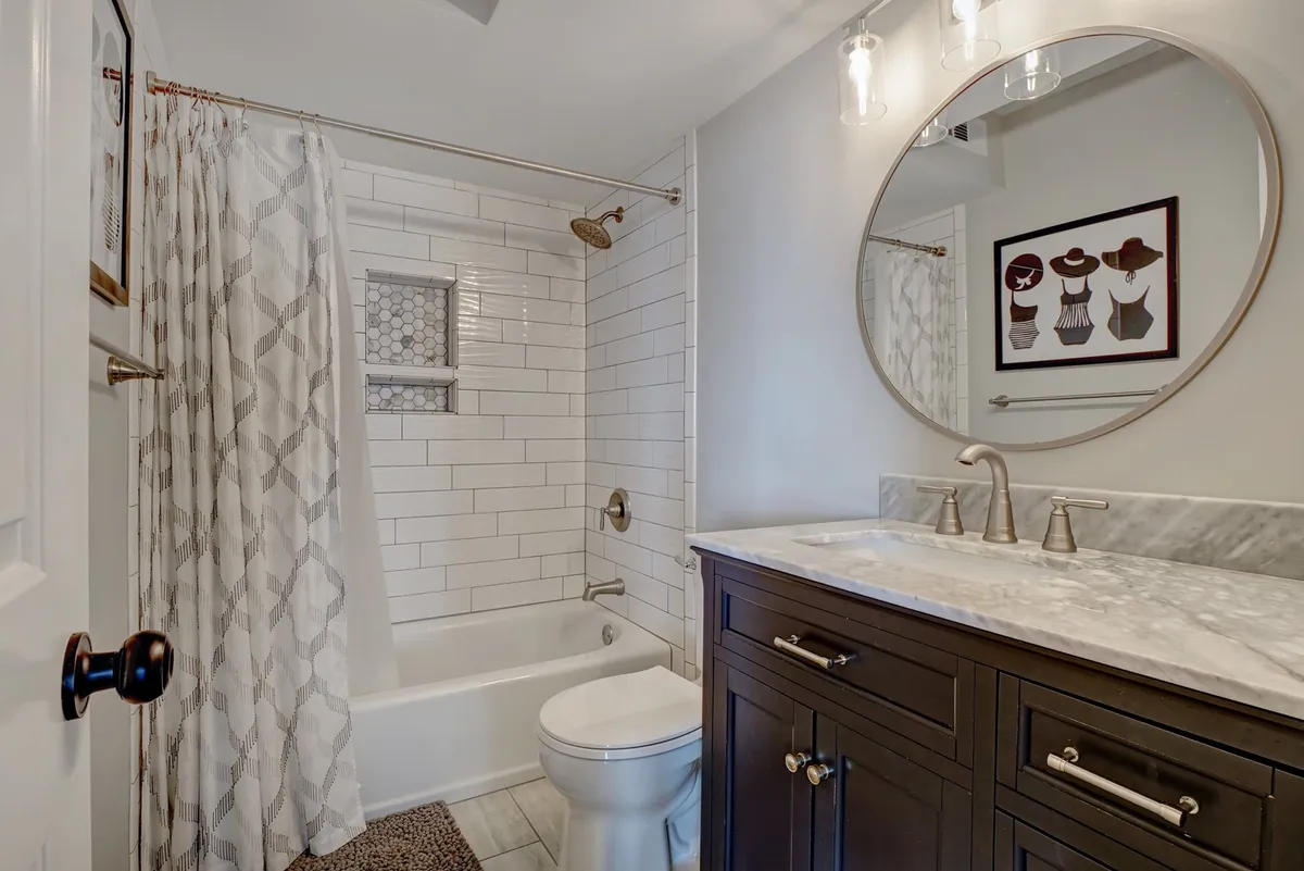 An inviting bathroom featuring a marble countertop, round mirror, spacious shower area, and a dark wooden vanity, creating a tranquil and luxurious atmosphere ideal for unwinding after a day at the beach.