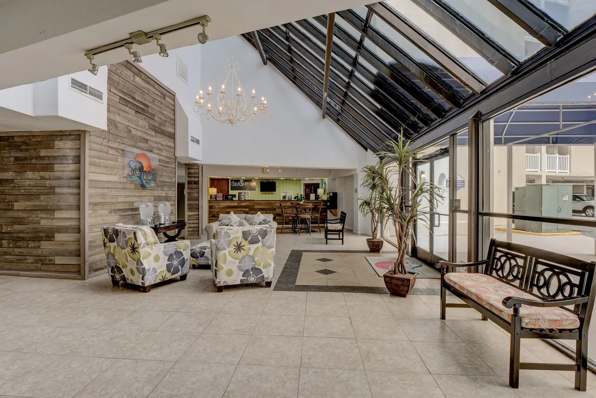 This image shows a welcoming lobby area with a chandelier overhead, a modern reception desk, comfortable seating, and large glass windows that let in abundant natural light. The space feels inviting and sets the tone for a seamless arrival experience.