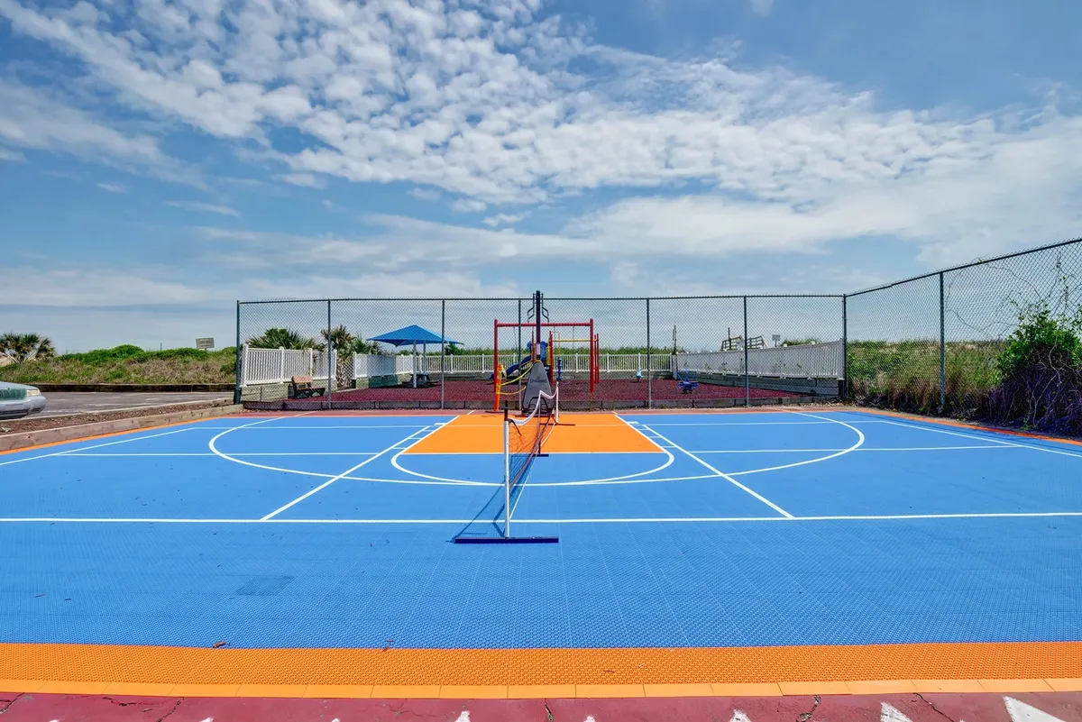 This lively exterior image centers on a brightly colored basketball court with a tennis net and features playground equipment in the background. Children can be seen playing, emphasizing active, communal recreation.