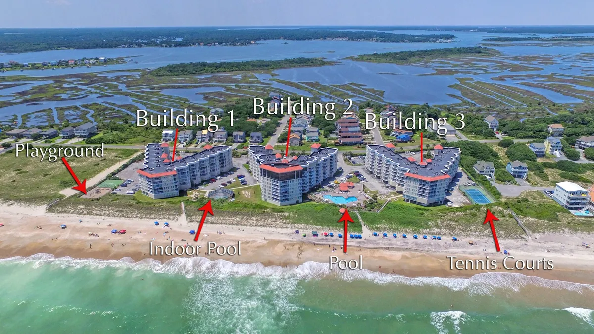 This aerial exterior shot captures the St. Regis property grounds, highlighting multiple family-friendly amenities including the pool, playground, tennis courts, and direct access to the beach. The photo conveys the property's vibrant atmosphere and the variety of activities available just steps from the condo.