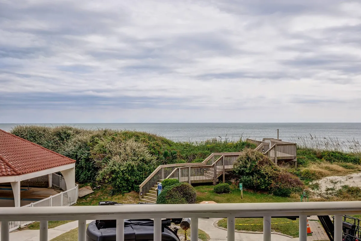 The image captures a tranquil scene featuring a staircase leading from lush, landscaped greenery down to a pristine sandy beach. Outdoor seating is positioned to offer sweeping, unobstructed views of the Atlantic Ocean, inviting guests to relax and take in the sunrise or enjoy meals al fresco. The atmosphere is peaceful and inviting, with natural elements blending seamlessly into the coastal surroundings.